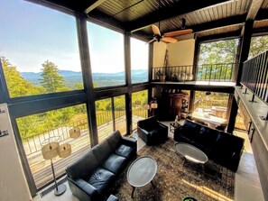 A spacious room with large windows offering a mountain view, a ceiling fan, and a cozy seating area with a sofa and coffee table.