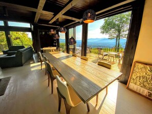 A modern dining area with a long table, chairs, pendant lights, and a view of the outdoors.