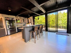 A modern kitchen with a central island, bar stools, and a large window overlooking greenery. - Rll (Whitefield)