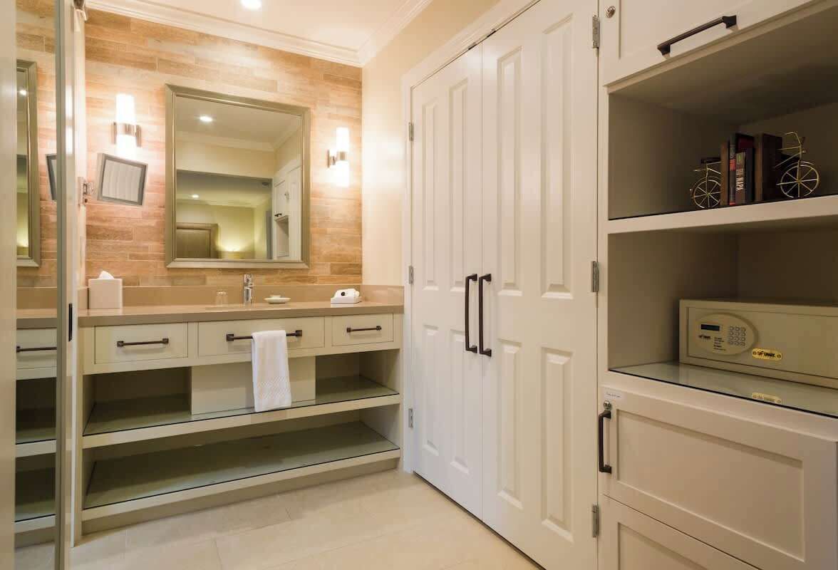 A modern bathroom with a large mirror, a vanity with a towel, and a shelf with books and a clock.