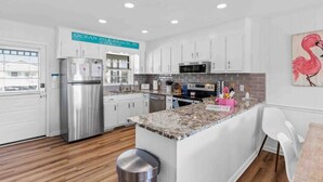 A modern kitchen with white cabinets, stainless steel appliances, and a granite countertop. - Pug Life - Walk to the Ocean! (Ocean Isle Beach)
