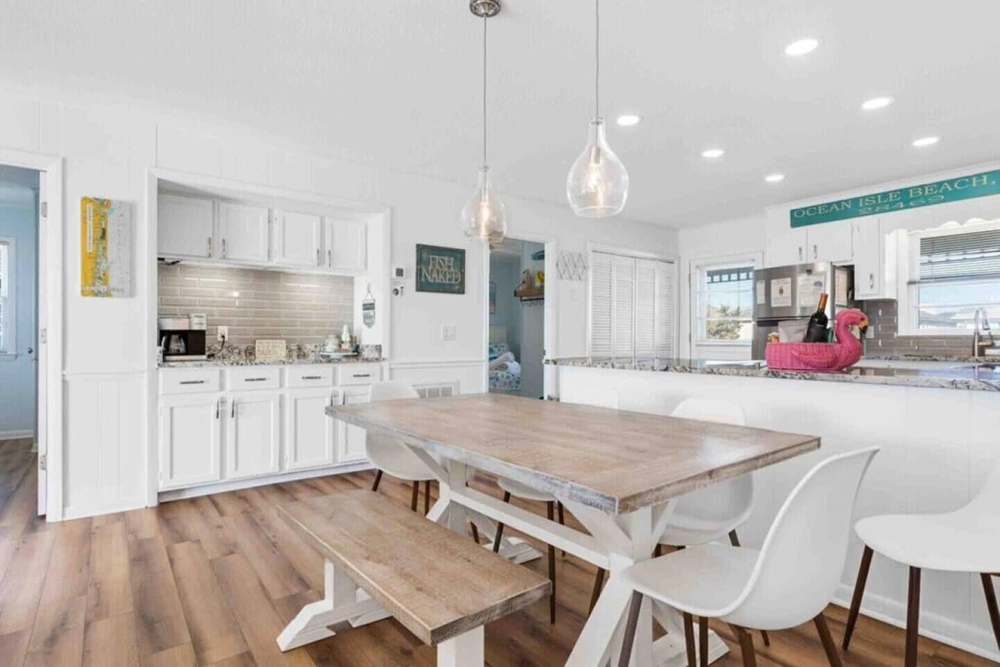 A modern kitchen with white cabinets, a wooden dining table, and pendant lighting.