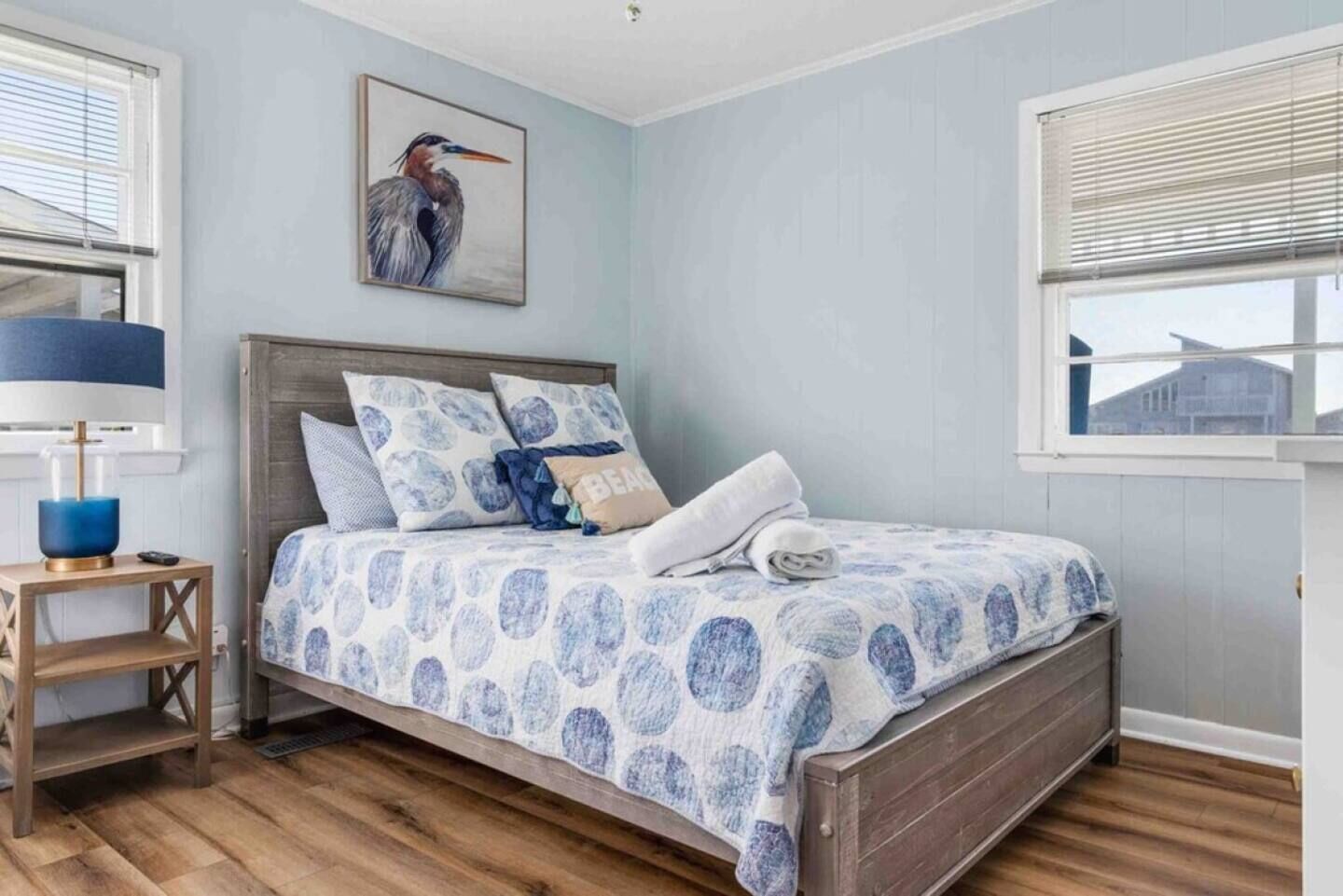 A bedroom with a bed, a nightstand, a lamp, a painting, and a window with blinds.
