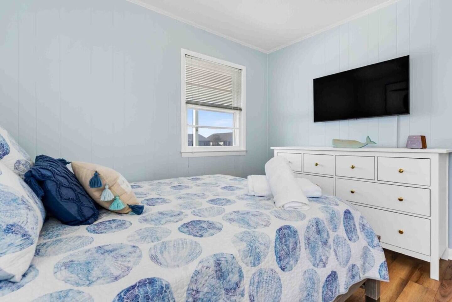 Un dormitorio con cama, cómoda, televisor y ventana.
