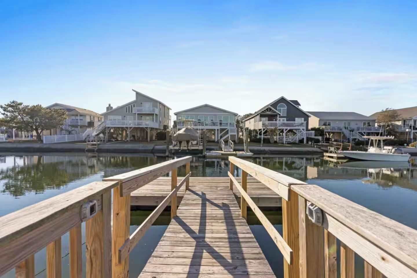 A wooden pier leading to a marina with houses on the other side.