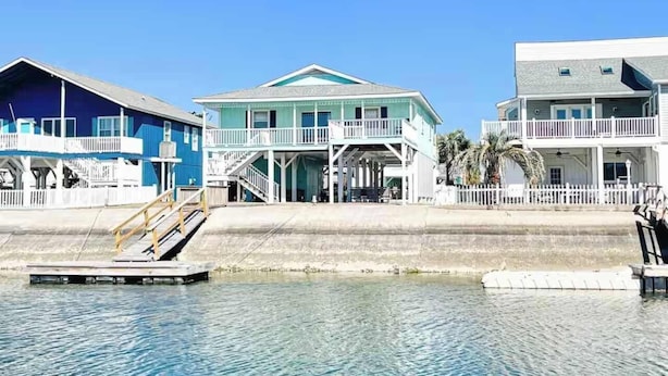 A beachfront property with a dock, a covered porch, and a staircase leading to the entrance. - Pug Life - Walk to the Ocean! (Ocean Isle Beach)