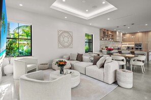 A modern living room with a sofa, chairs, a coffee table, and a dining area with a kitchen in the background. - Villa Banyan by Rove Travel 7BR Home W/mini Golf (North Miami Beach)