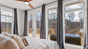 A bedroom with a large bed, a ceiling fan, and a view of a deck and outdoor area through large windows. - Primrose - Cave Run Lake OR Red River Gorge KY (Wellington)