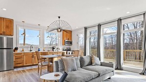 A modern kitchen with wooden cabinets, a stainless steel refrigerator, and a dining area with a gray sofa and a small table. - Primrose - Cave Run Lake OR Red River Gorge KY (Wellington)