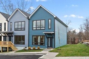 A modern two-story residential building with a blue exterior, large windows, and a front deck.