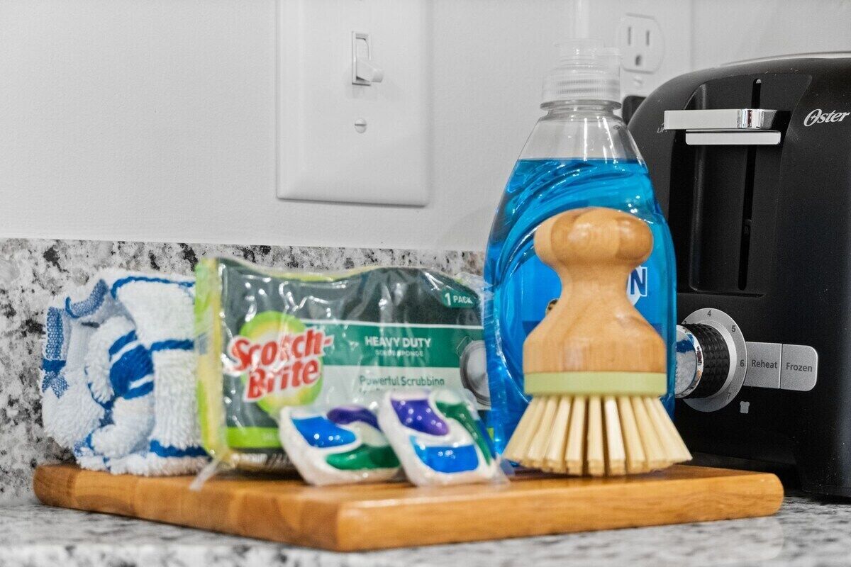 A kitchen counter with a dishcloth, a bottle of dish soap, a brush, and a coffee maker.