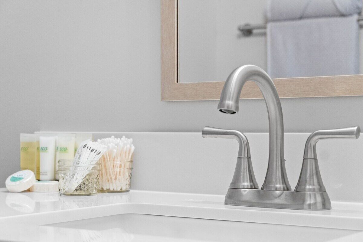 Une salle de bain moderne avec un robinet élégant en métal, un grand miroir et un plan de toilette où sont posés les articles de toilette.