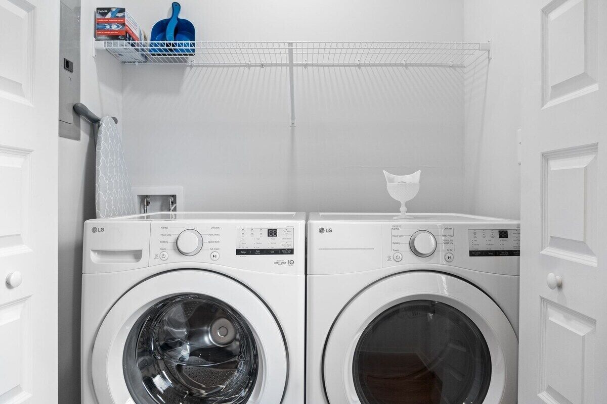 A laundry area with two white LG front-loading washing machines, a metal shelf with laundry supplies, and a white door.