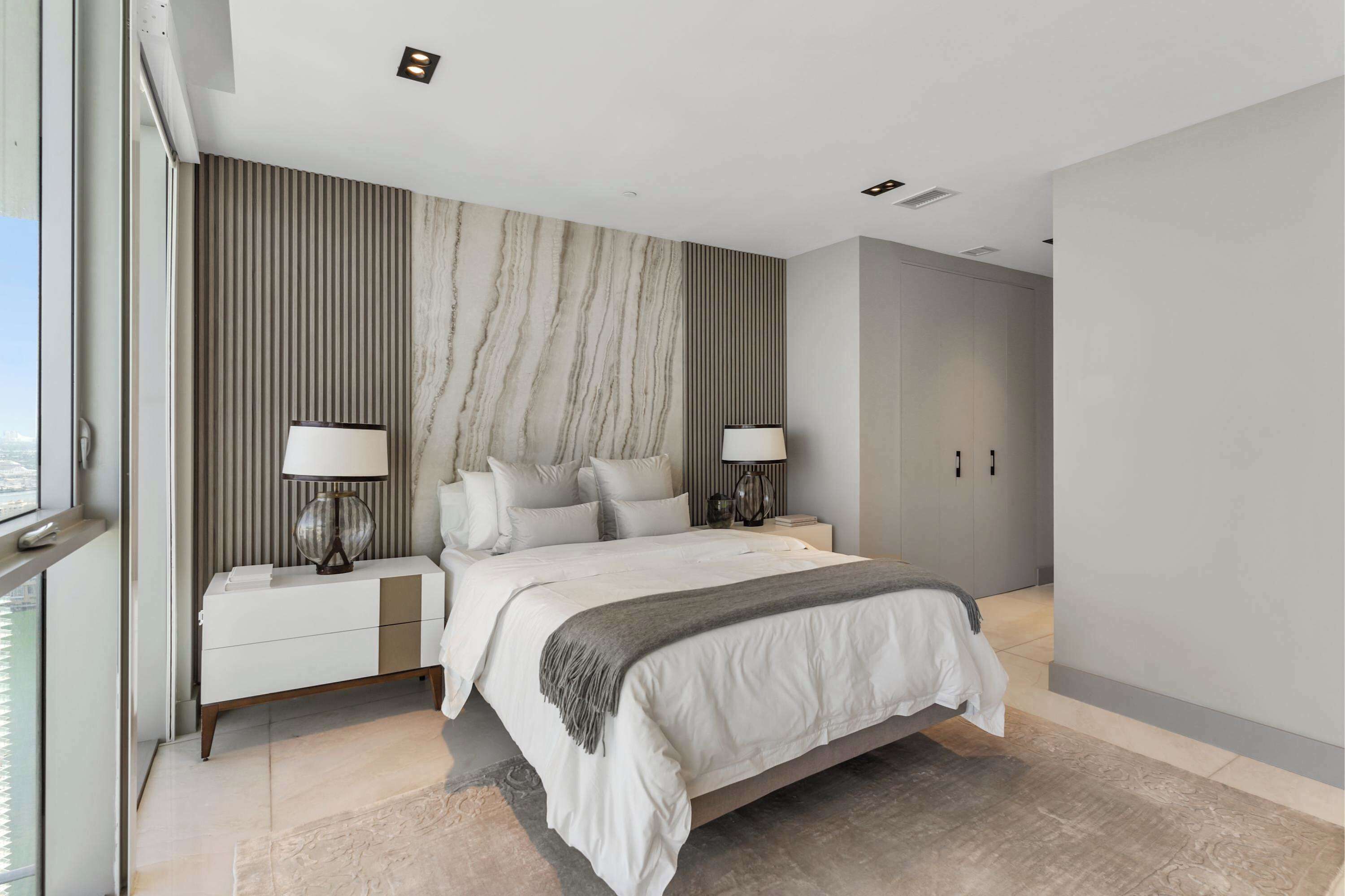 A modern bedroom with a large bed, two bedside tables, a nightstand, and a view of the city.