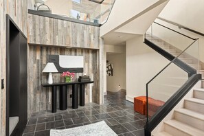 Ein modernes Interieur mit einer Wandpaneinung aus Holz, einem schwarzen Konsolentisch mit Lampe, einer Blumenvase und einer Treppe mit Glasgeländern.