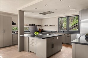 Eine moderne Küche mit Kochinsel, integrierten Geräten und einem großen Fenster mit Blick ins Freie.