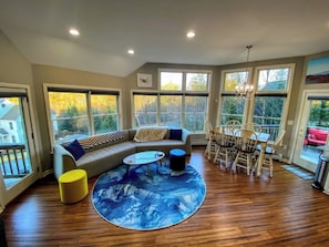 Uma sala de estar espaçosa com uma janela grande, um sofá modular, uma mesa de jantar com cadeiras e uma mesa de centro redonda.