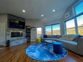 Una sala de estar con chimenea de piedra, un sofá, una mesa de centro y ventanas amplias con vistas.