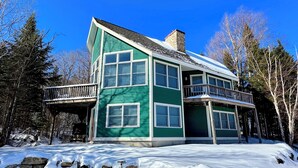 Una casa de dos pisos con fachada verde, ventanas grandes y un balcón.