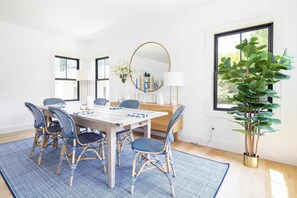A dining area with a wooden table, blue and white patterned chairs, a round mirror, and a potted plant. - Sandpoint by Rove Travel 6BR Family Home w Pool (Shelter Island)