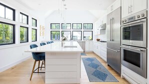 A modern kitchen with a central island, stainless steel appliances, and large windows. - Sandpoint by Rove Travel 6BR Family Home w Pool (Shelter Island)
