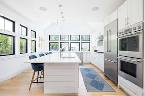Uma cozinha moderna com ilha central, eletrodomésticos de aço inoxidável e grandes janelas.