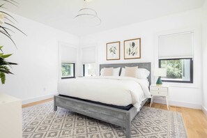 A bedroom with a bed, bedside tables, a patterned rug, and framed artwork on the wall. - Sandpoint by Rove Travel 6BR Family Home w Pool (Shelter Island)