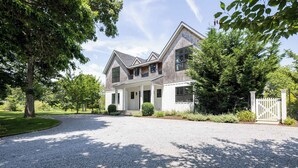 A two-story house with a gravel driveway, a front porch, and a white fence. - Sandpoint by Rove Travel 6BR Family Home w Pool (Shelter Island)