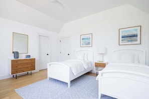 Quarto com duas camas, cômoda, mesa de cabeceira e uma porta.