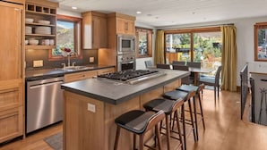 A modern kitchen with wooden cabinets, stainless steel appliances, and a central island with bar stools. - Snowline Lodge 4BR Home With Hot Tub, Pool & BBQ (Aspen)