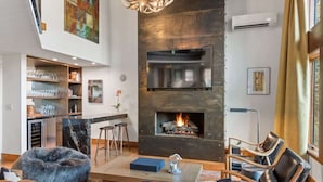 A modern living room with a fireplace, seating area, and a kitchen with bar seating. - Snowline Lodge 4BR Home With Hot Tub, Pool & BBQ (Aspen)