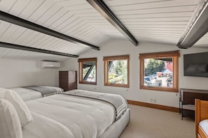 Un dormitorio con dos camas, un escritorio y un televisor. Hay tres ventanas con vistas al exterior.