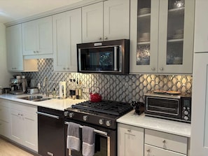 A modern kitchen with grey cabinets, a black stove, a microwave, and a toaster.