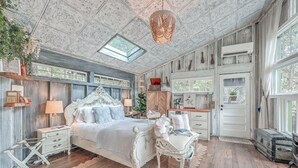 Ein Schlafzimmer mit einem großen Bett, einem Schreibtisch, einem Stuhl, einem Fenster und einer Decke mit einem Oberlicht.