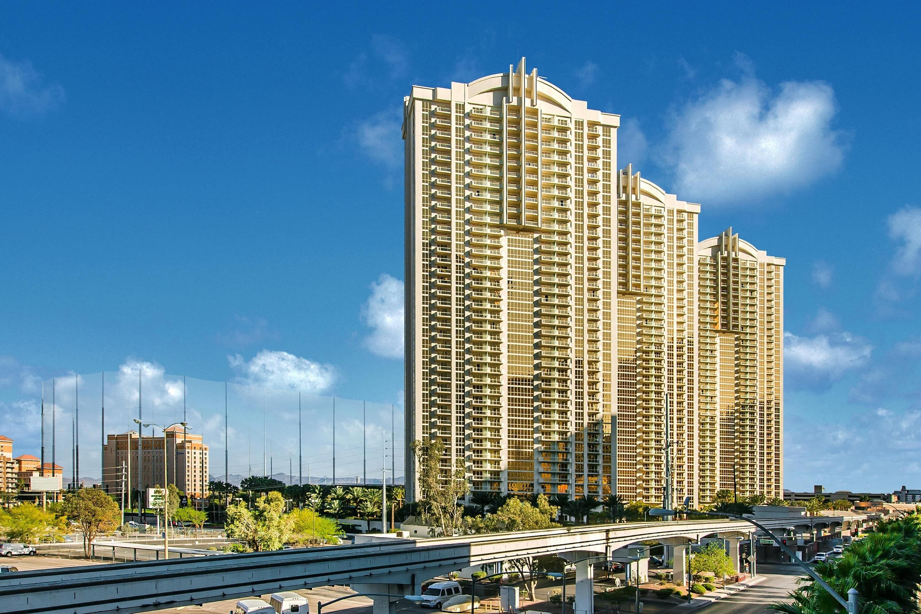 A high-rise building with multiple balconies, a clear sky, and a highway in the foreground.