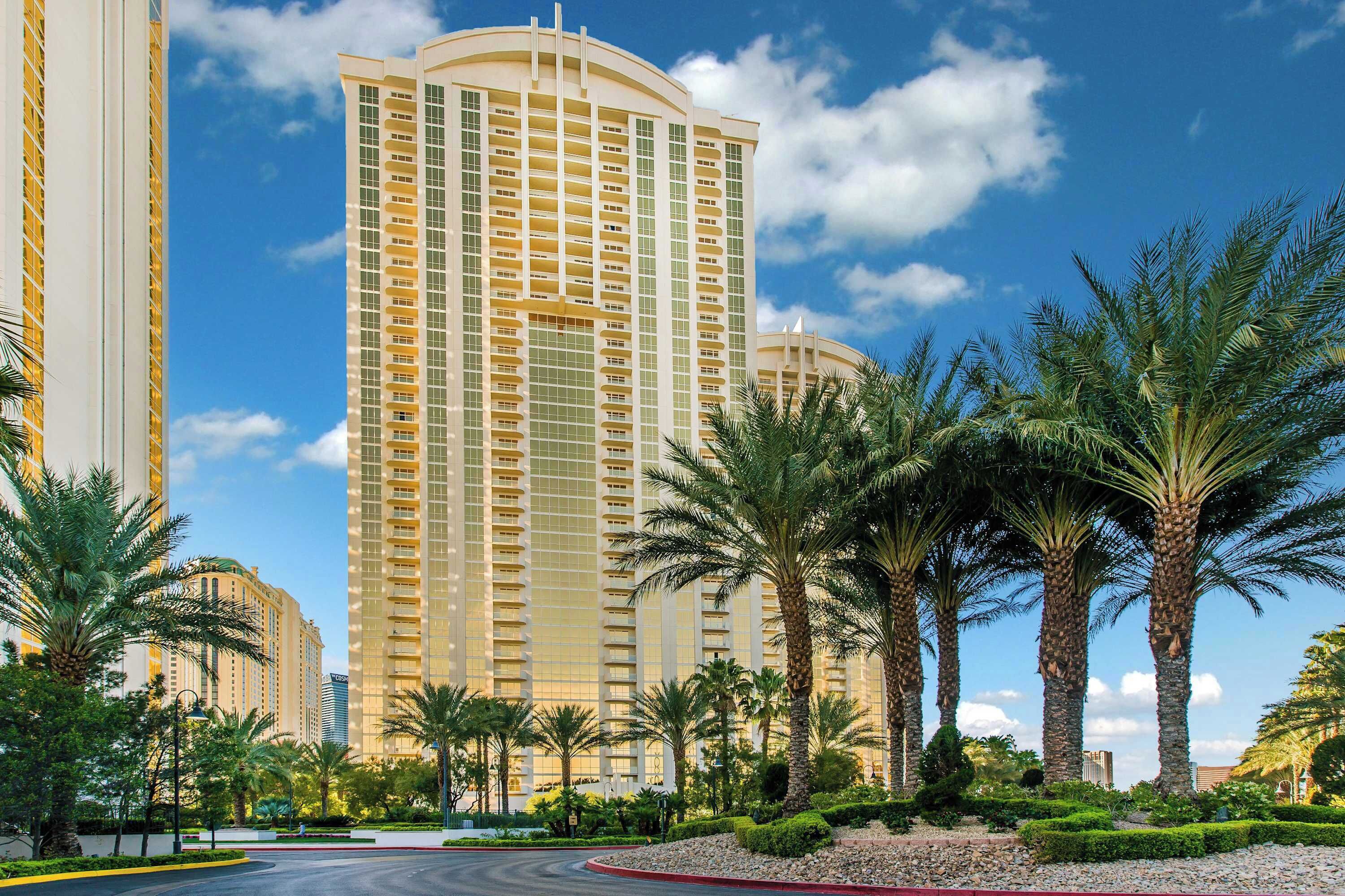 A high-rise hotel with a curved facade, surrounded by palm trees and well-maintained landscaping.