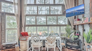 A cozy room with a large window, a television, a wooden table, and chairs. - The Charleston Treehouse (Wadmalaw Island)