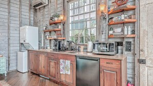 A rustic kitchen with wooden cabinets, a dishwasher, a microwave, and shelves with various kitchen items. - The Charleston Treehouse (Wadmalaw Island)