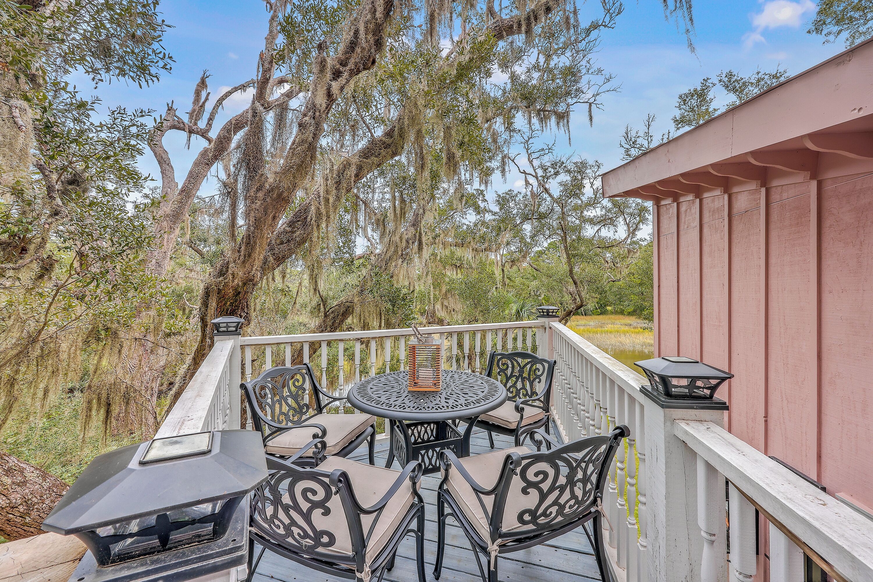 Une terrasse avec une table ronde et des chaises, entourée d’arbres et d’un bâtiment.
