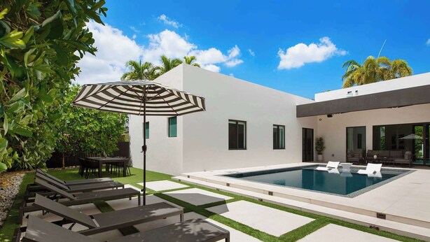 Ein moderner Poolbereich im Freien mit Liegestühlen, einer überdachten Lounge und blauem Himmel.