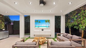 Ein moderner Außenbereich mit Fernseher, Sitzgelegenheiten und Blick auf einen tropischen Strand.