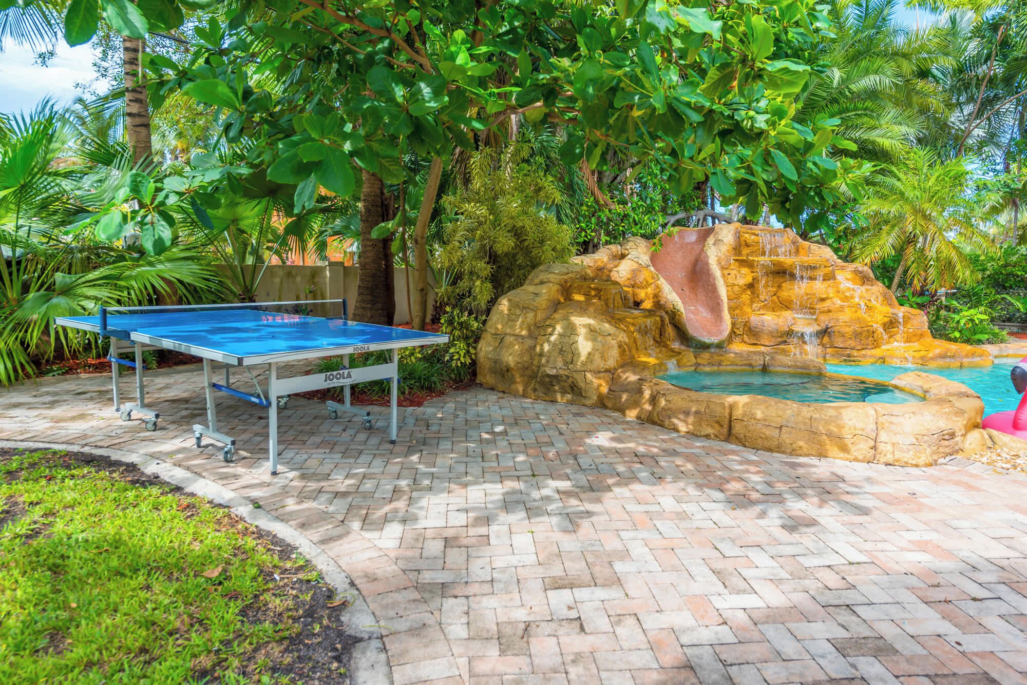 A ping pong table, a rock waterfall, and a pool in a landscaped outdoor area.