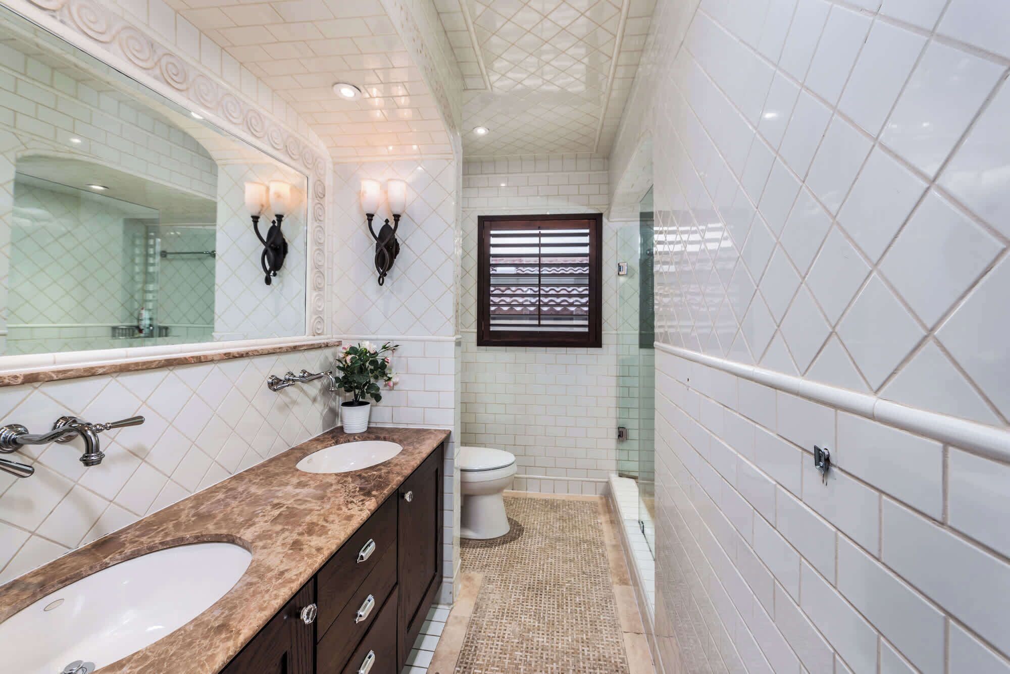 A bathroom with a double sink vanity, a large mirror, a toilet, and a shower area.