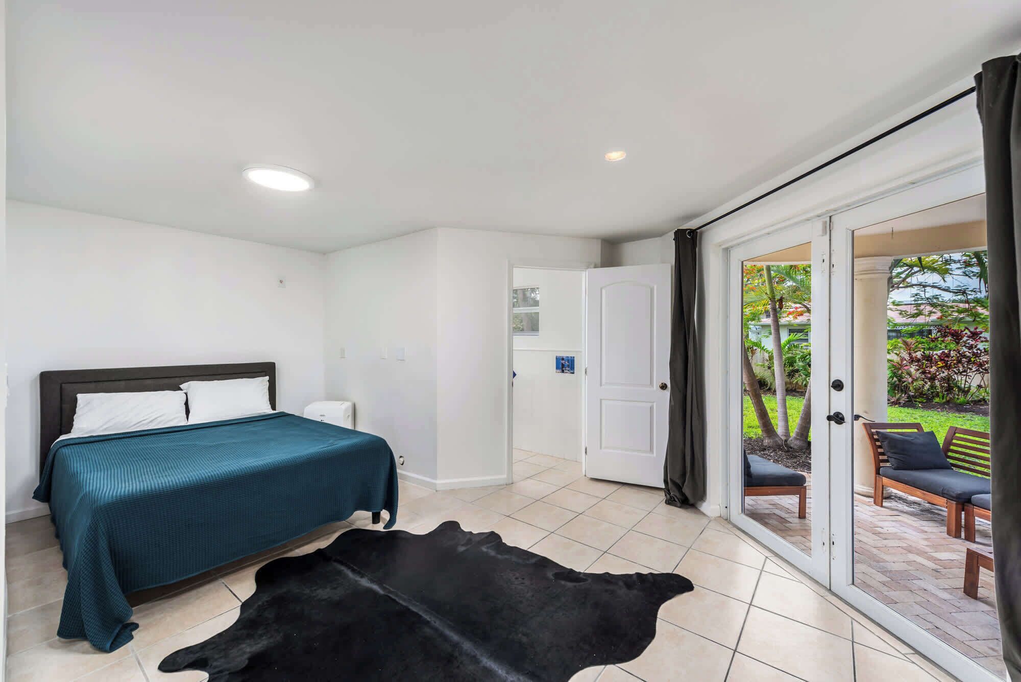 A bedroom with a bed, a white door, and a view of an outdoor patio with a chair and a table.
