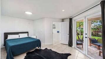 A bedroom with a bed, a white door, and a view of an outdoor patio with a chair and a table.