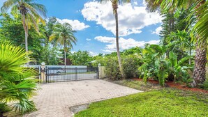 A paved entrance to a property with a gated driveway, surrounded by lush greenery and palm trees. - Villa Justina by Rove Villa W/pool & Hot Tub (Miami)