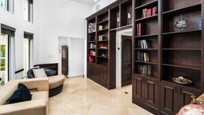 A spacious living room with a large dark wooden bookshelf, a beige sofa, and a door leading to another room. - Villa Justina by Rove Villa W/pool & Hot Tub (Miami)