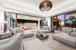 Ein modernes Wohnzimmer mit einem Ecksofa, einem Couchtisch und einem großen Fenster mit Blick ins Freie.