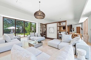 Ein geräumiges Wohnzimmer mit großem Fenster, einer modernen Kronleuchter und einem Essbereich mit Holztisch und -stühlen.