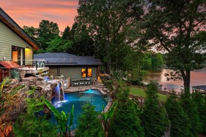 Ein Haus mit Swimmingpool, Wasserfall und Blick auf einen See im Abendrot.